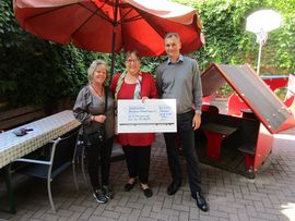 2 Frauen und ein Mann stehen im Hof und halten lächelnd einen Scheck hoch