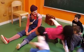 Clownin Pipilotta sitzt mit mehreren Kindern lachend auf dem Boden
